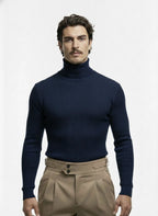 Man wearing a navy turtleneck sweater and beige pants on a white background