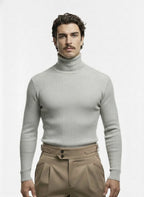 Man wearing a light gray turtleneck sweater and beige pants on a white background