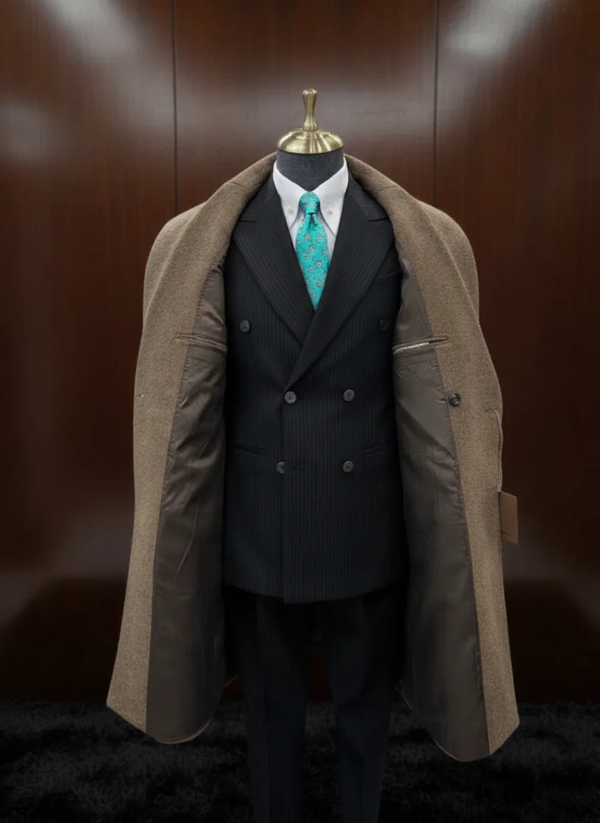 Mannequin wearing a dark suit with a green tie and a brown overcoat against a wooden panel background